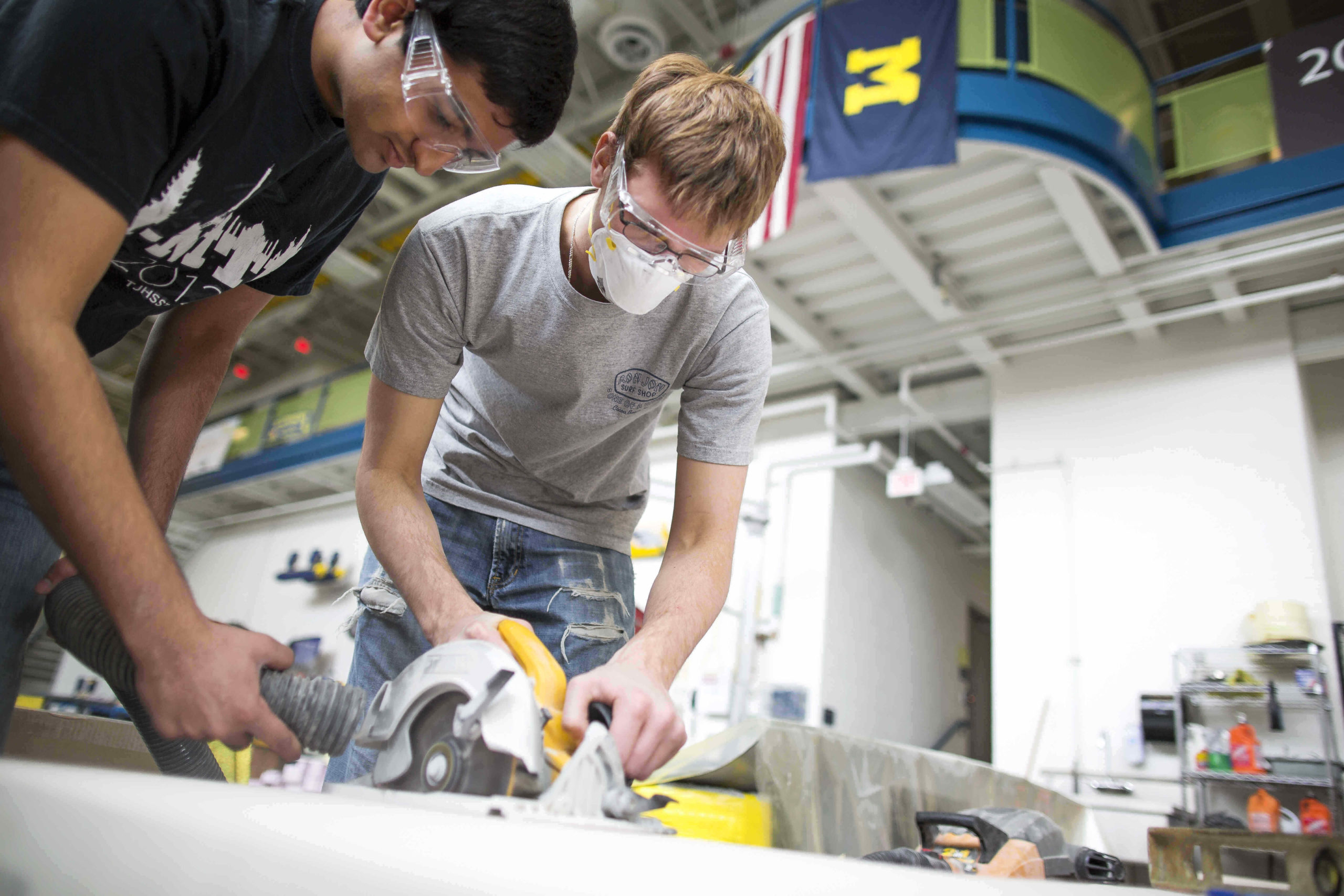 Two students in safety gear working with a saw in the Wilson Center