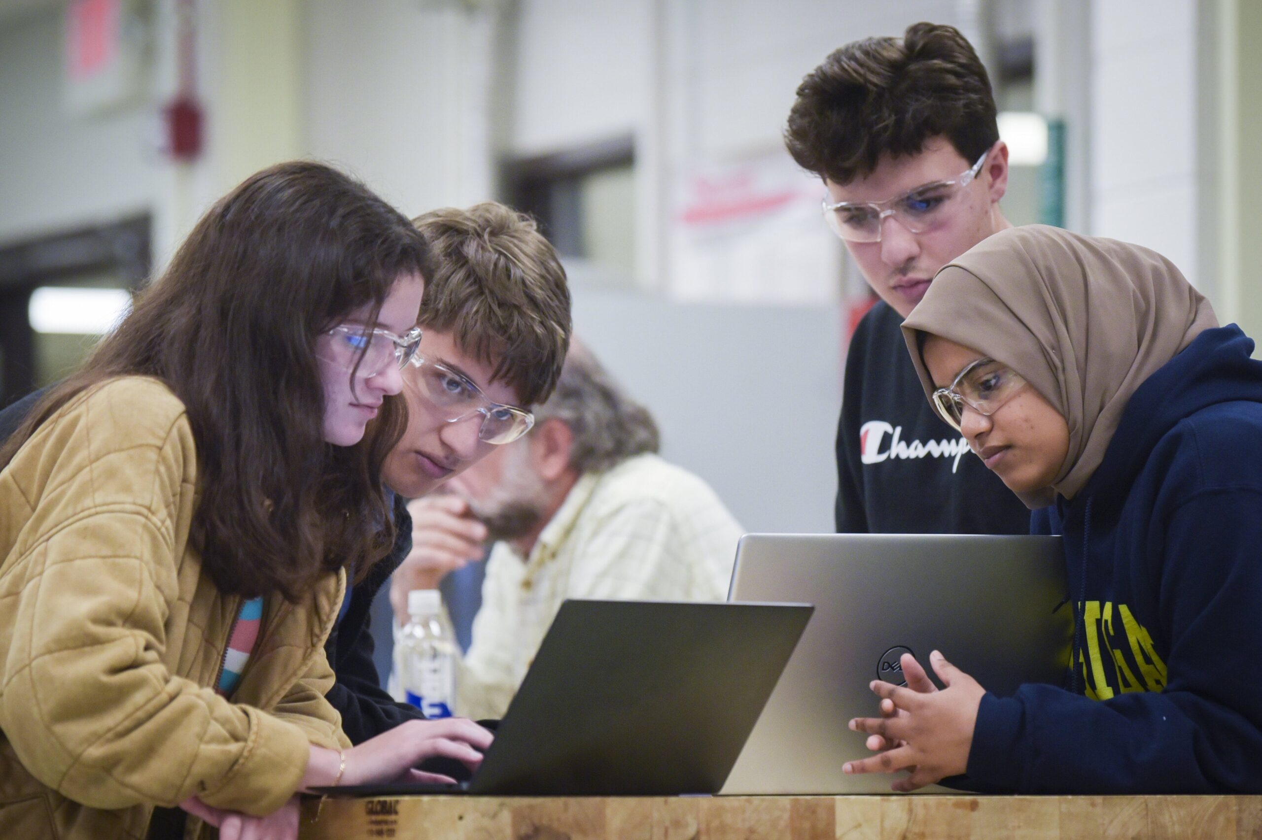 Four students in goggles huddle over laptop 